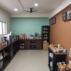 Suasana kantor yang nyaman dengan karyawan sedang berinteraksi di area pantry atau coffee corner, menunjukkan pentingnya fasilitas relaksasi di kantor baru. Ada mesin kopi dan snack di meja, dengan beberapa karyawan tersenyum.